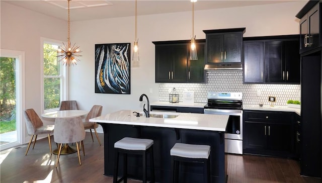 kitchen featuring decorative light fixtures, light countertops, decorative backsplash, an island with sink, and stainless steel electric range