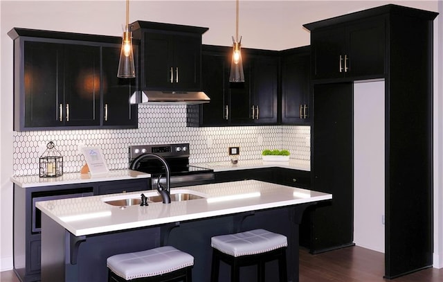 kitchen featuring light countertops, dark cabinets, a center island with sink, and under cabinet range hood