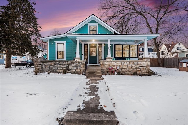 view of front of home featuring covered porch, stone siding, and fence