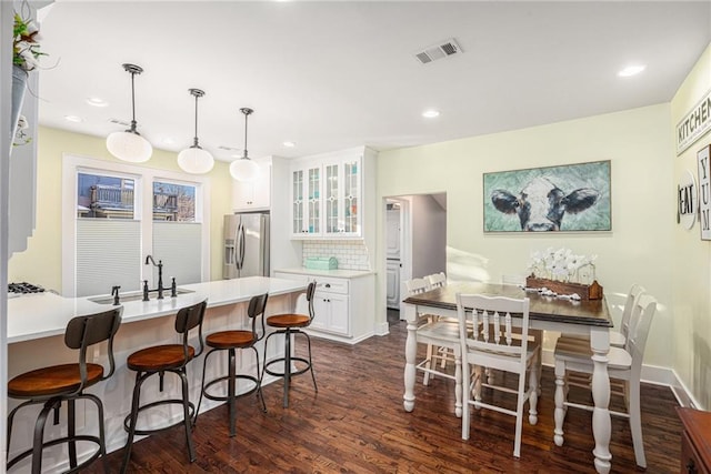 kitchen with visible vents, a breakfast bar, a sink, white cabinets, and stainless steel fridge