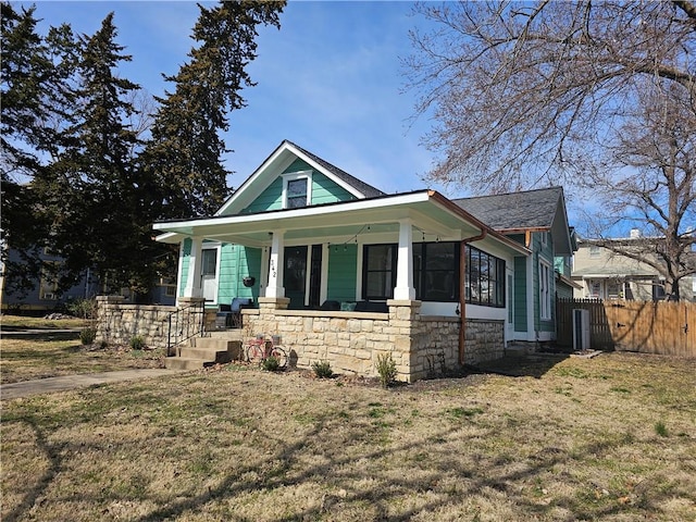 bungalow-style home featuring stone siding, a porch, a front lawn, and fence