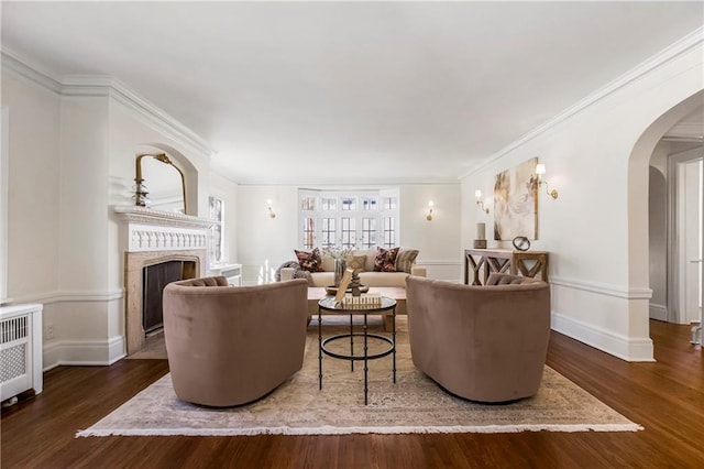 living room featuring arched walkways, a fireplace, baseboards, and wood finished floors