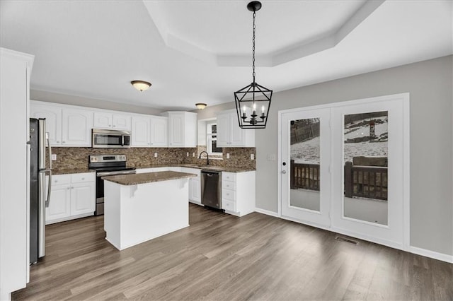 kitchen with a center island, a tray ceiling, decorative light fixtures, stainless steel appliances, and white cabinets