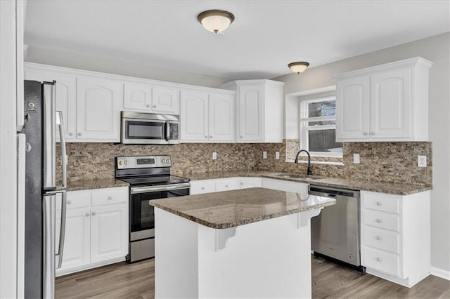 kitchen with a kitchen island, a sink, white cabinets, appliances with stainless steel finishes, and dark stone counters