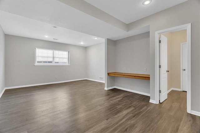 spare room featuring recessed lighting, dark wood finished floors, built in desk, and baseboards