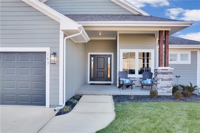 property entrance featuring covered porch, a yard, roof with shingles, and a garage