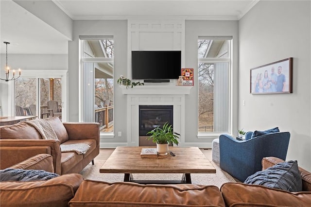 living area featuring baseboards, a glass covered fireplace, ornamental molding, wood finished floors, and a chandelier