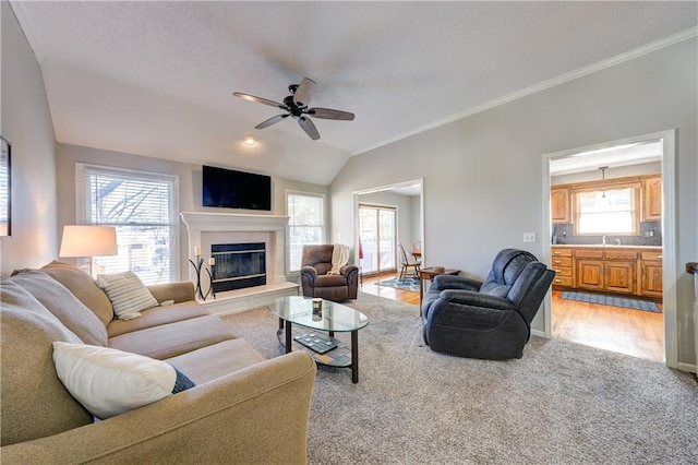 living room featuring lofted ceiling, ceiling fan, light colored carpet, ornamental molding, and a glass covered fireplace