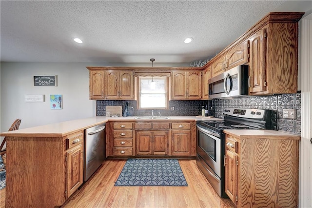 kitchen with a peninsula, brown cabinetry, appliances with stainless steel finishes, and light countertops