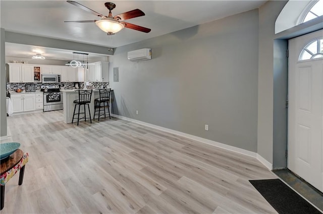 interior space with a wall mounted air conditioner, a kitchen breakfast bar, tasteful backsplash, white cabinetry, and appliances with stainless steel finishes