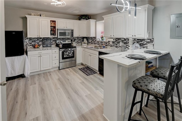 kitchen with a breakfast bar area, a peninsula, electric panel, black appliances, and white cabinetry