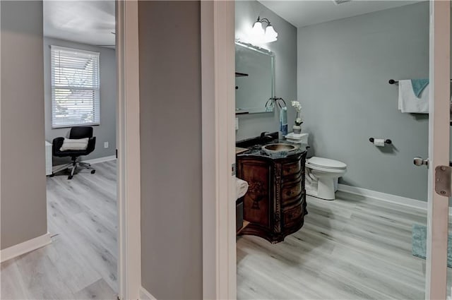 bathroom featuring toilet, vanity, baseboards, and wood finished floors