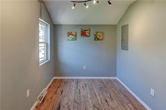 spare room featuring visible vents, electric panel, wood finished floors, baseboards, and vaulted ceiling