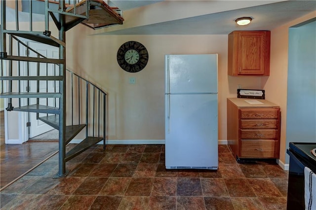 kitchen with brown cabinets, black range with electric stovetop, stone finish flooring, freestanding refrigerator, and baseboards