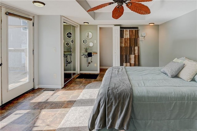 bedroom with a tray ceiling, stone finish flooring, baseboards, and a ceiling fan