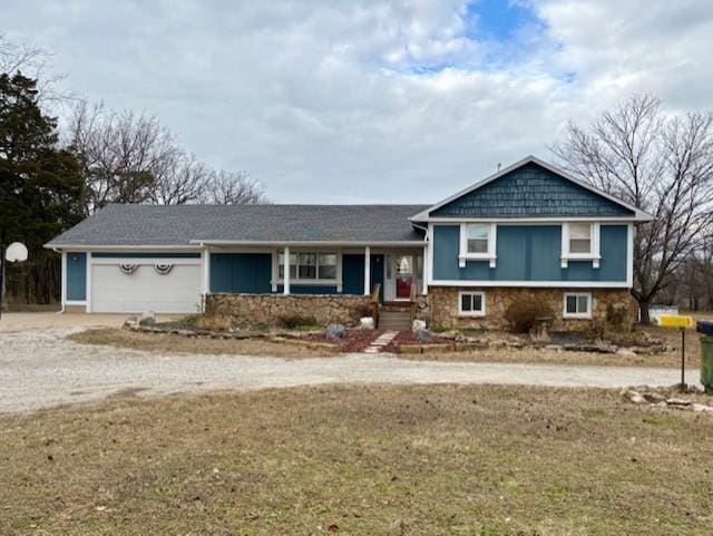 split level home featuring dirt driveway, stone siding, an attached garage, and a front yard