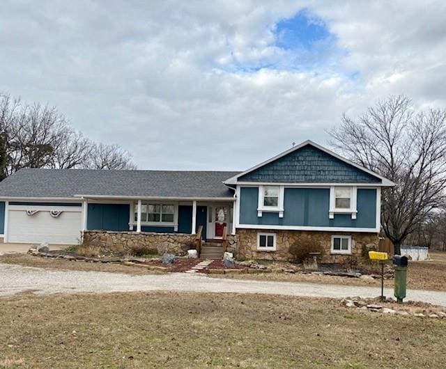 tri-level home featuring an attached garage, stone siding, concrete driveway, and a front yard