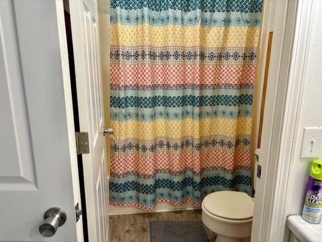 bathroom featuring curtained shower, toilet, and wood finished floors