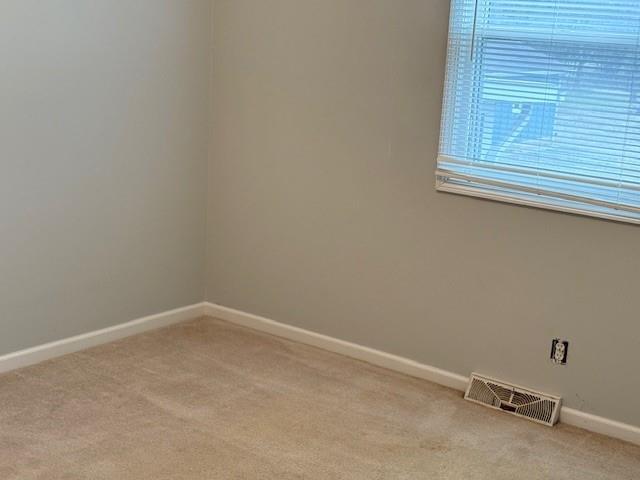 spare room with light carpet, visible vents, and baseboards