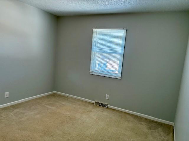 empty room with light carpet, baseboards, visible vents, and a textured ceiling