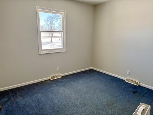 empty room with visible vents, dark carpet, and baseboards