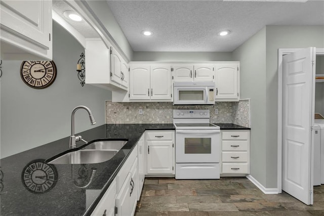 kitchen with white appliances, white cabinetry, dark stone counters, and a sink