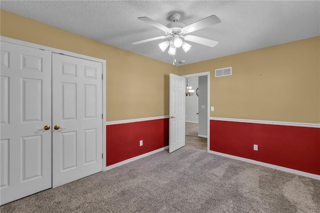 unfurnished bedroom featuring a textured ceiling, light carpet, visible vents, baseboards, and a closet