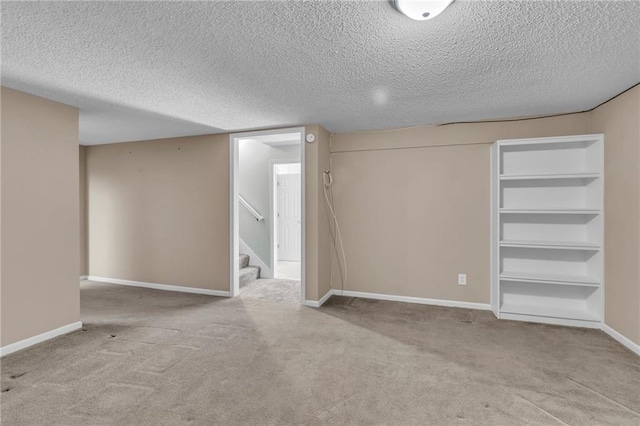 finished below grade area featuring light colored carpet, a textured ceiling, baseboards, and stairs