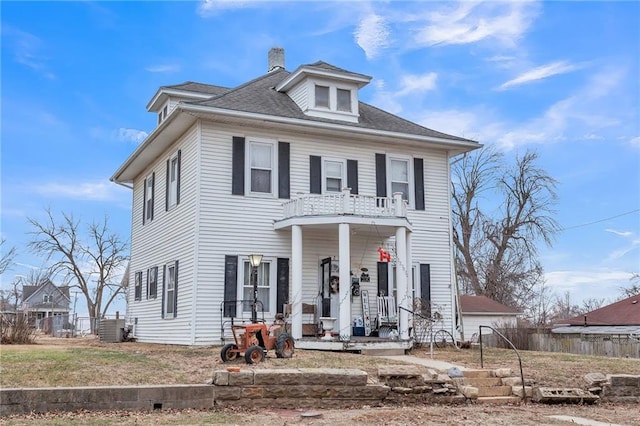 traditional style home with a chimney, covered porch, central AC unit, fence, and a balcony