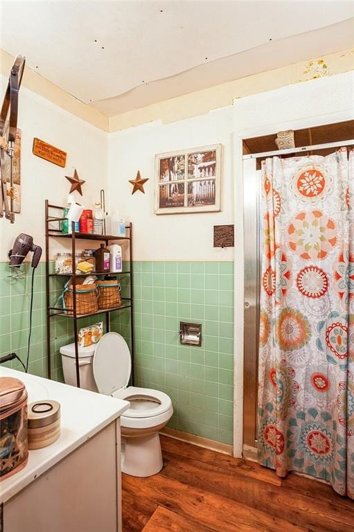 bathroom with toilet, wainscoting, wood finished floors, and tile walls