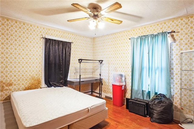 bedroom with ceiling fan, wood finished floors, baseboards, wallpapered walls, and crown molding