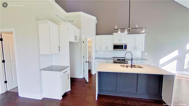 kitchen with stainless steel appliances, a kitchen island with sink, pendant lighting, and white cabinets