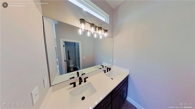 full bath with double vanity, a sink, toilet, and baseboards