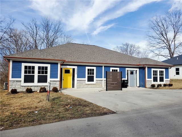 view of front facade featuring stone siding, a shingled roof, a front lawn, and driveway