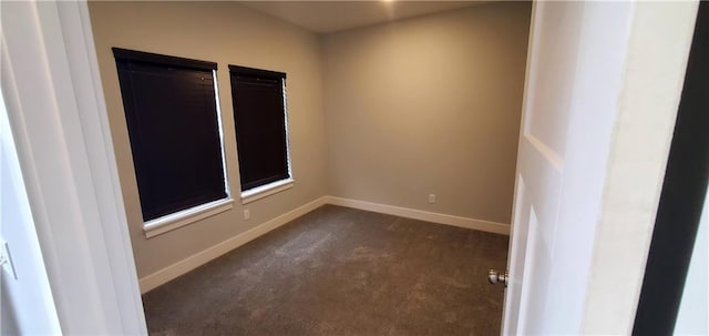 spare room featuring dark colored carpet and baseboards