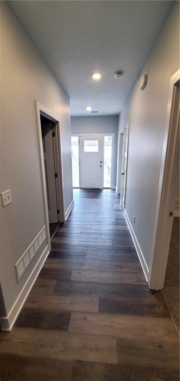 hallway with baseboards, visible vents, and dark wood-style flooring