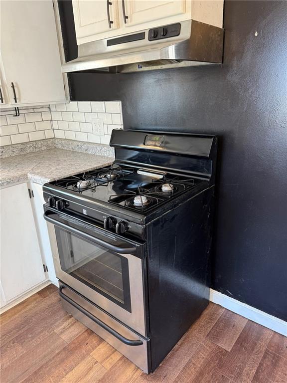 kitchen with light wood finished floors, tasteful backsplash, stainless steel gas range oven, light countertops, and under cabinet range hood