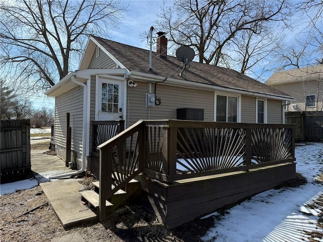 rear view of property featuring a shingled roof, a chimney, fence, and a wooden deck