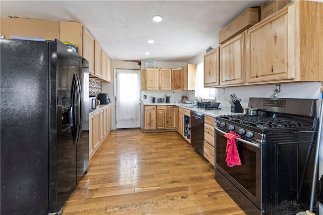 kitchen with stainless steel range with gas cooktop, light brown cabinetry, dishwashing machine, and black fridge