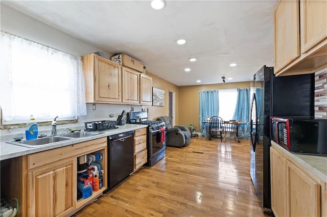 kitchen featuring light wood finished floors, a sink, light brown cabinetry, black appliances, and a wealth of natural light