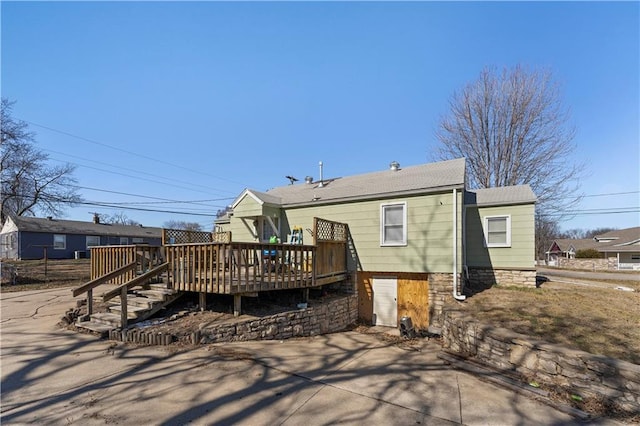 rear view of property featuring concrete driveway, an attached garage, and a wooden deck