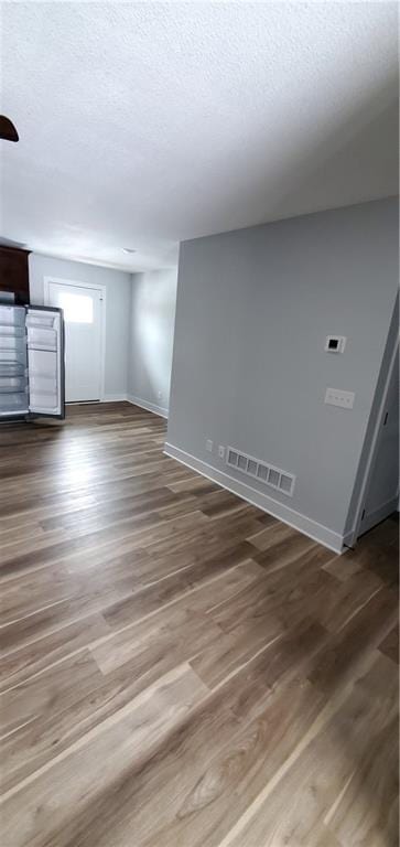 spare room featuring visible vents, a textured ceiling, baseboards, and wood finished floors