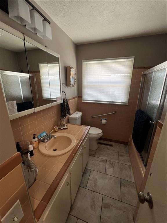 bathroom with a textured ceiling, wainscoting, a shower with door, and vanity