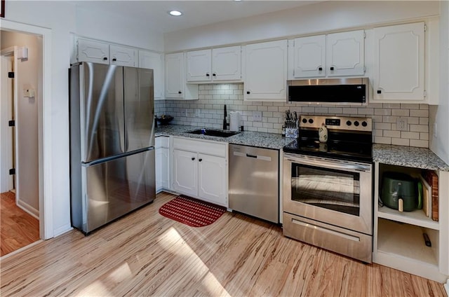 kitchen with light stone counters, a sink, white cabinets, appliances with stainless steel finishes, and light wood finished floors