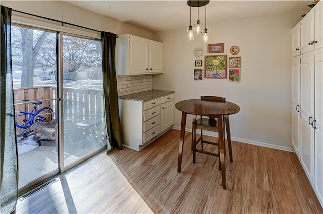 kitchen featuring visible vents, baseboards, white cabinets, decorative backsplash, and light wood finished floors