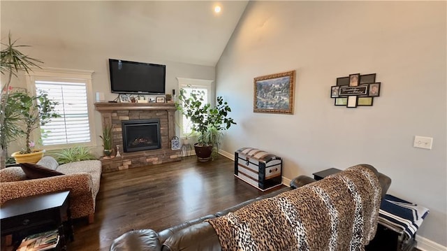 living area featuring high vaulted ceiling, a stone fireplace, dark wood finished floors, and baseboards