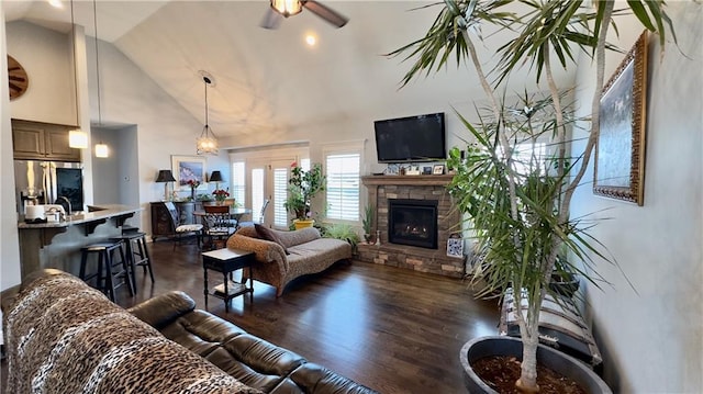 living room featuring high vaulted ceiling, a stone fireplace, dark wood finished floors, and a ceiling fan