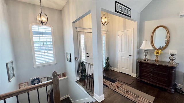 entryway with dark wood finished floors, a notable chandelier, vaulted ceiling, and baseboards