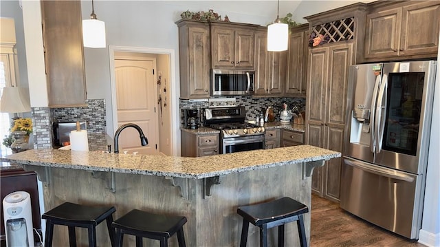 kitchen featuring stainless steel appliances, hanging light fixtures, a sink, light stone countertops, and a peninsula