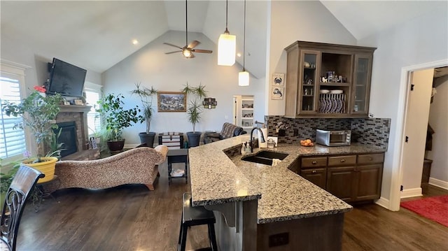 kitchen featuring a breakfast bar, glass insert cabinets, open floor plan, a sink, and dark brown cabinets